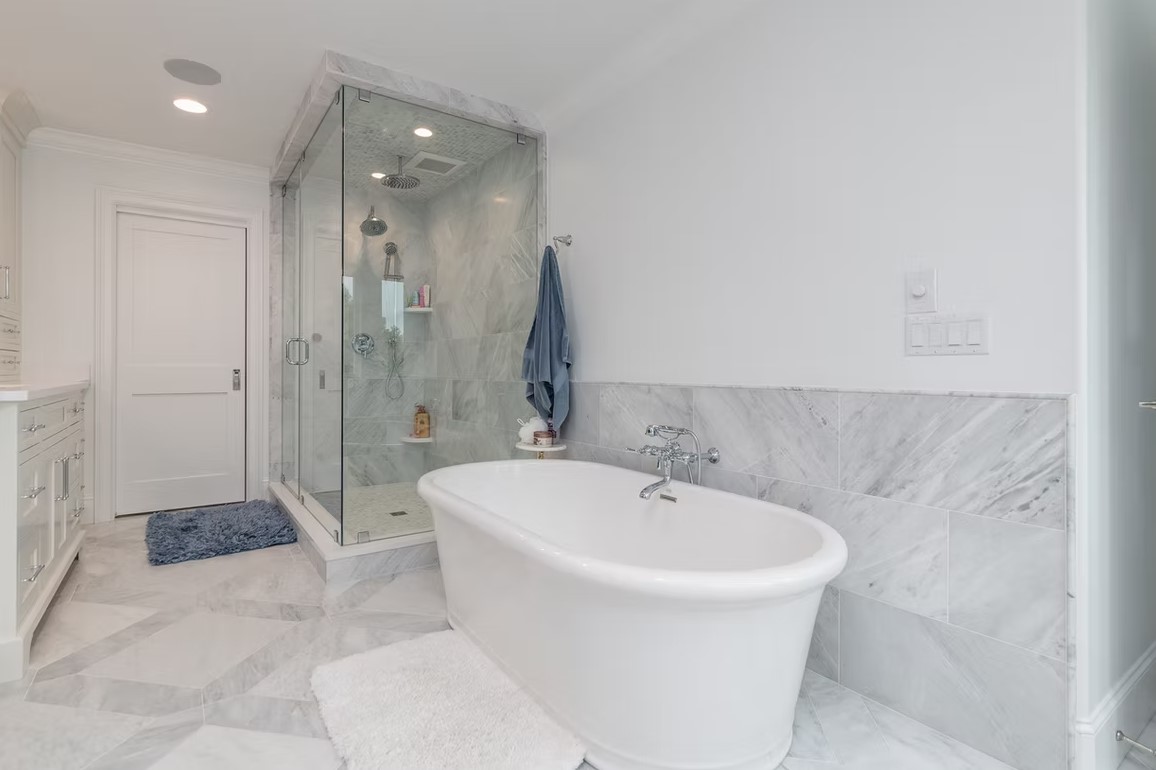 Luxury bathroom featuring a freestanding white soaking tub, marble flooring, and a large window with privacy shutters.
