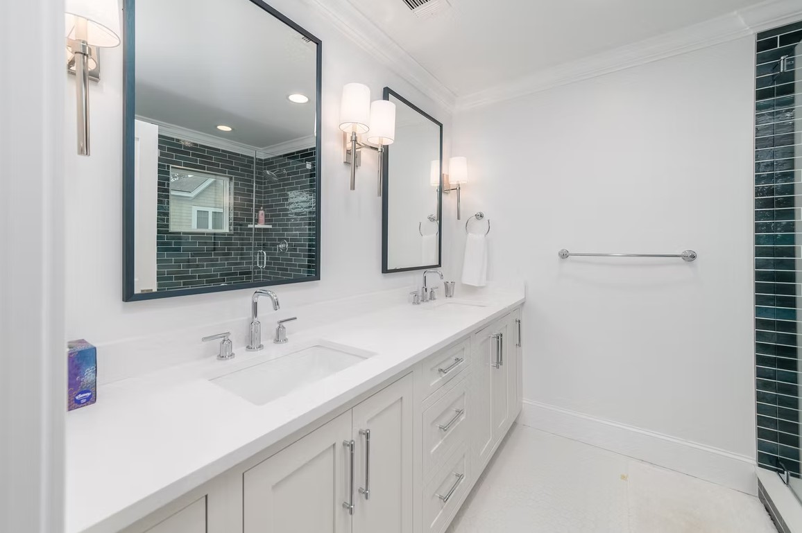 Classic master bathroom featuring a built-in alcove bathtub with marble surround, white cabinetry, and a large window overlooking lush greenery.